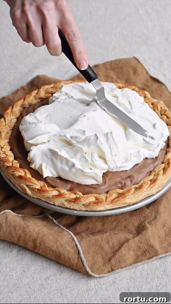 Whipped cream being spread over a chocolate pie with an offset spatula.