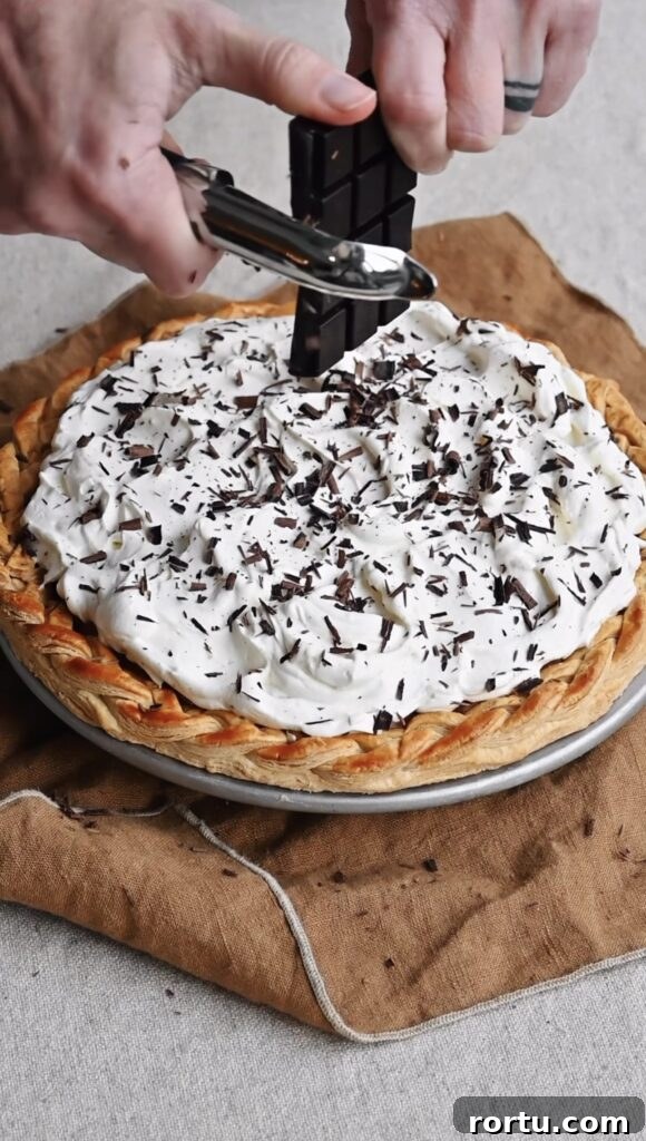 A chocolate bar being grated over a whipped cream topped pie to make chocolate shavings.