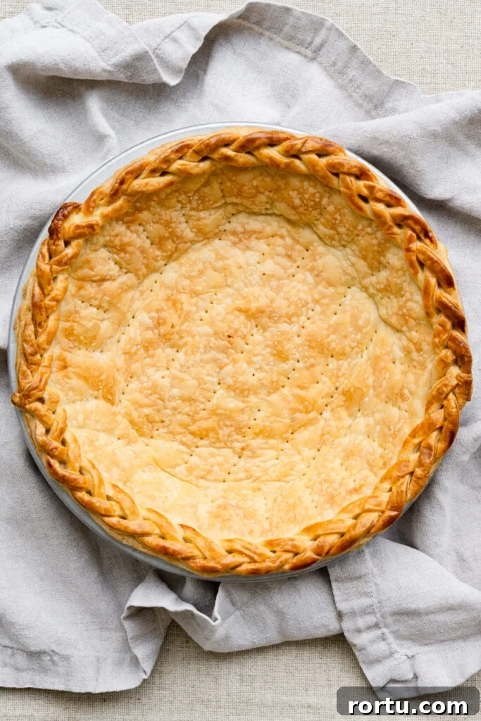 Overhead of a fully blind baked pie crust with a braided edge on a linen napkin.