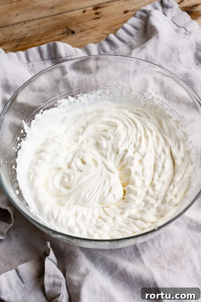 Vanilla whipped cream in a large glass bowl on a table cloth.