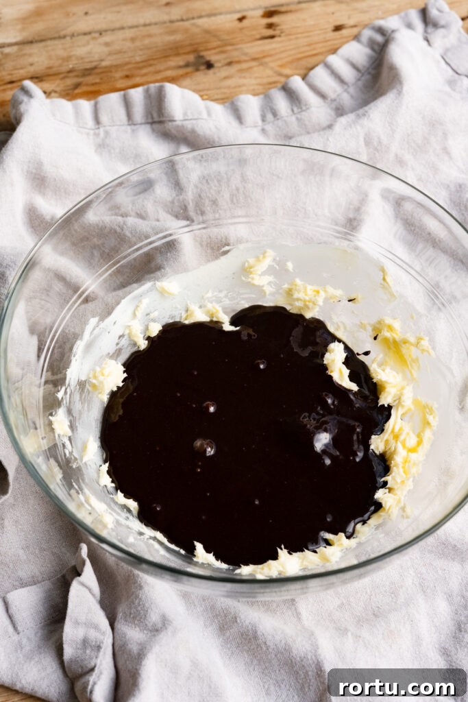Dark chocolate egg mixture poured on top of softened butter in a large mixing bowl.