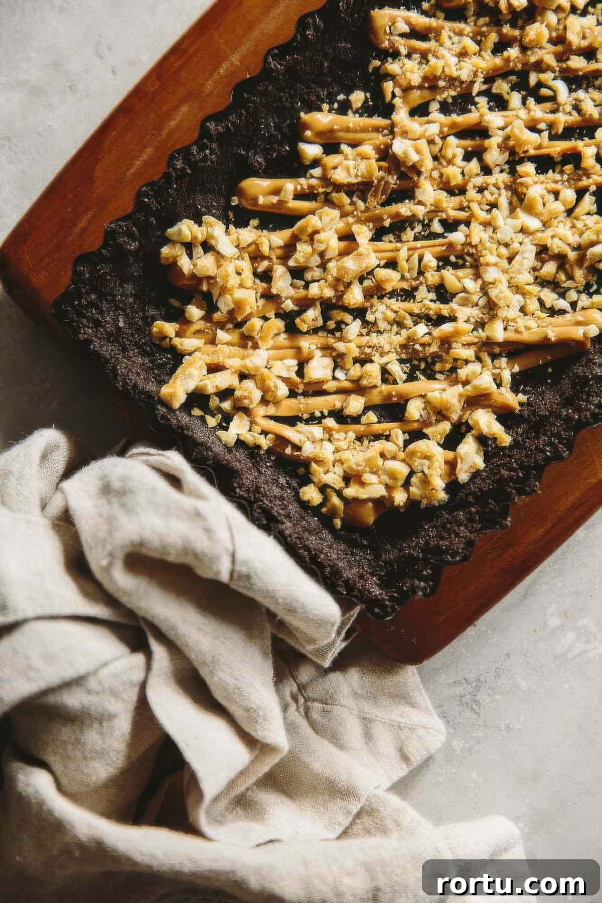 a chocolate ganache tart with chopped peanut brittle and a drizzle of warmed peanut butter before being filled with ganache
