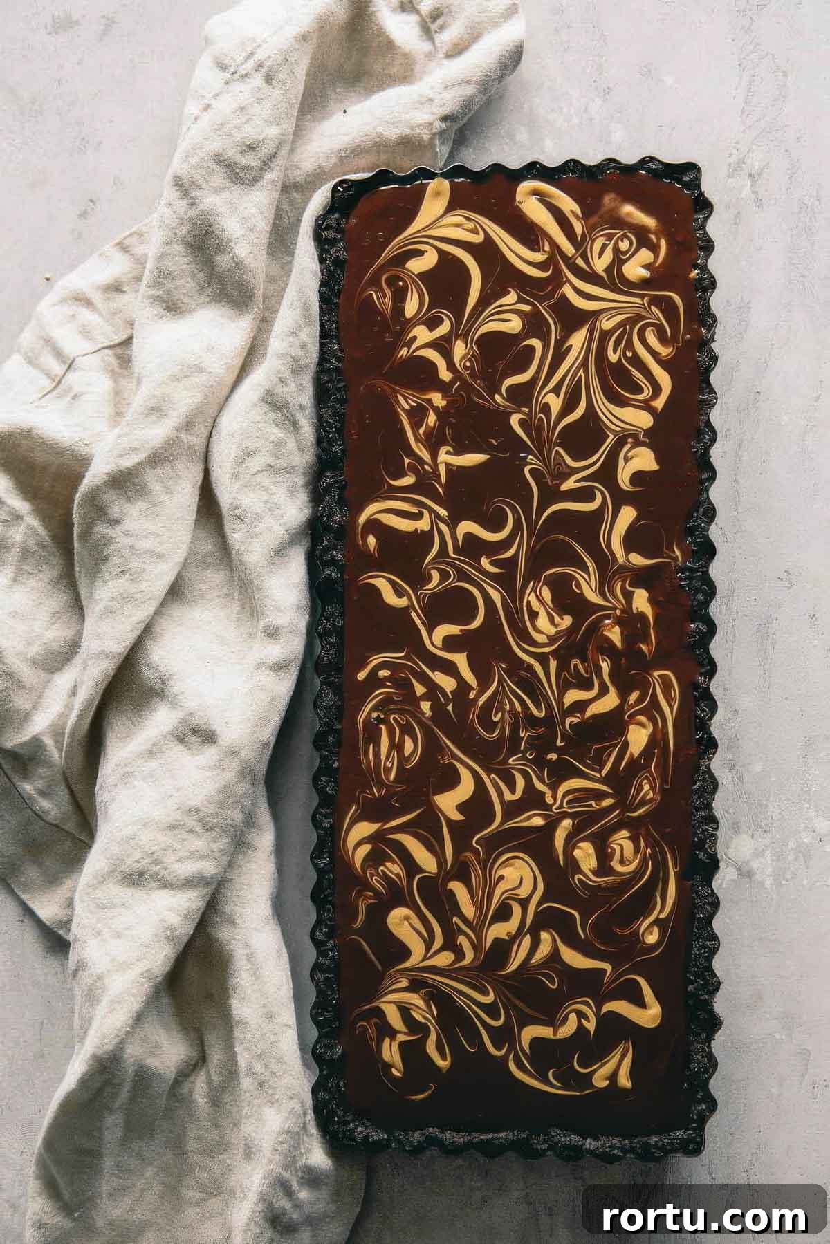 a top-down view of a chocolate ganache tart with a decorative peanut butter swirl next to a beige towel