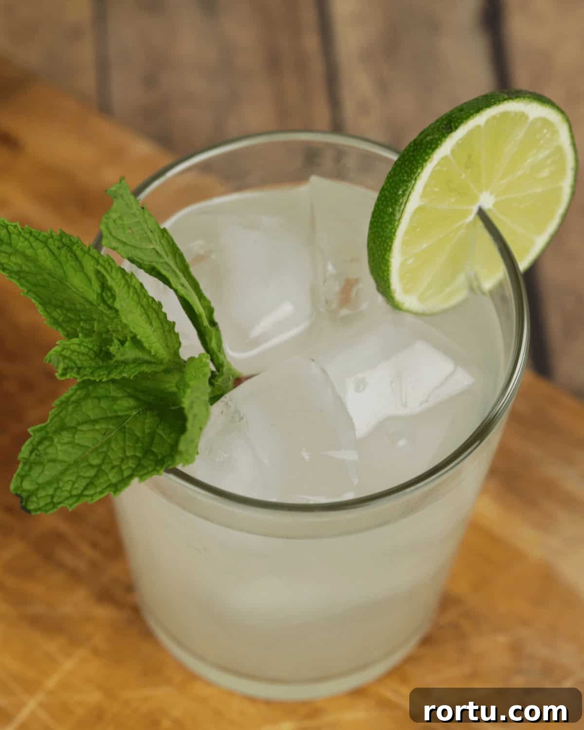 A refreshing lime moonshine drink garnished with a sprig of mint on a wooden surface.