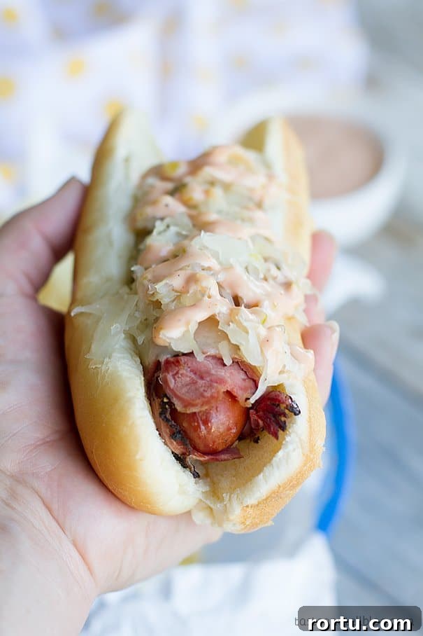Hand holding a Pastrami Wrapped Hot Dog.