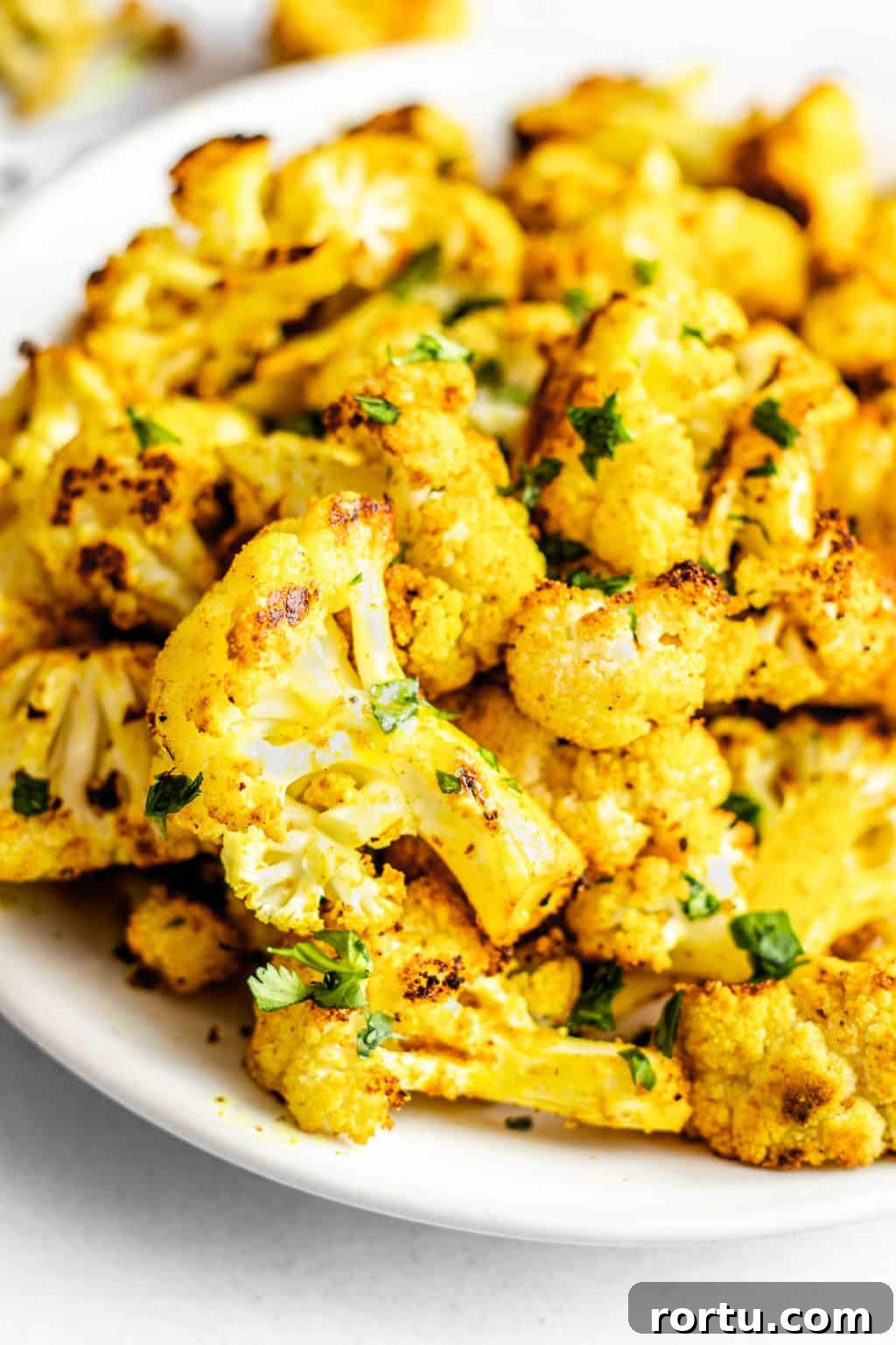 Crispy Roasted Cauliflower with Curried Spice Rub 2 close up on a pile of roasted curried cauliflower on a white plate.