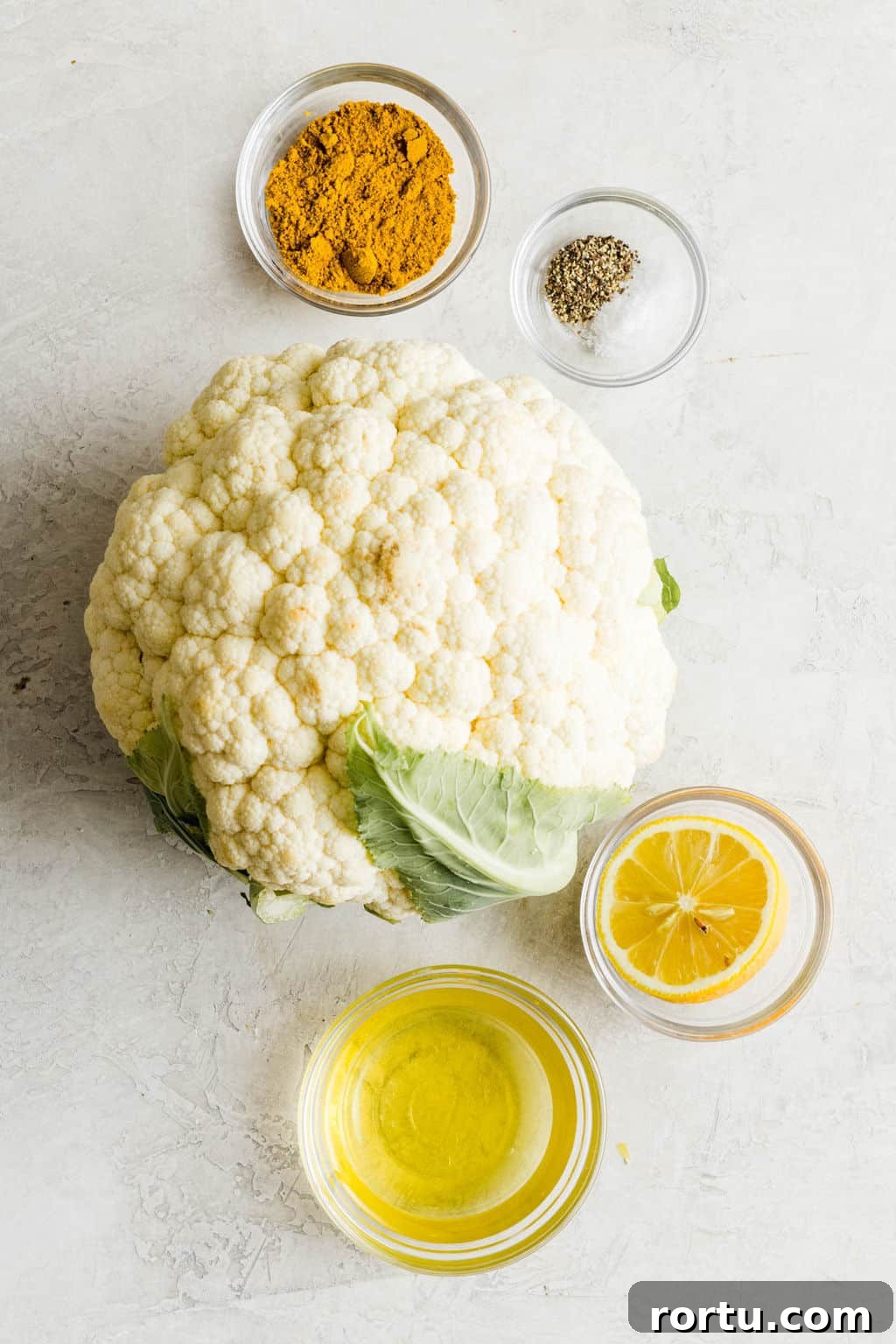Crispy Roasted Cauliflower with Curried Spice Rub 3 a head of cauliflower next to small glass bowls filled with oil, lemon, pepper, and yellow curry powder.