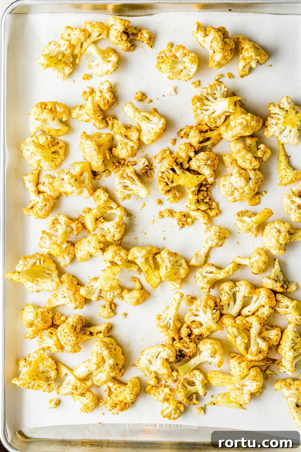 Crispy Roasted Cauliflower with Curried Spice Rub 5 Yellow curry-seasoned cauliflower florets on a parchment lined baking sheet.