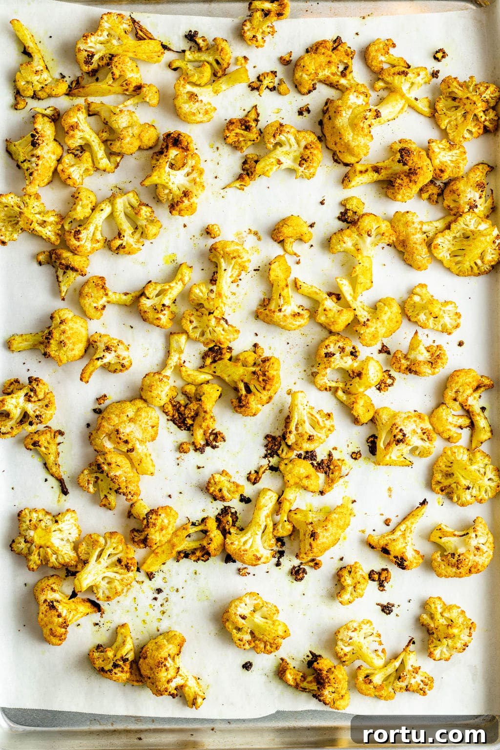 Crispy Roasted Cauliflower with Curried Spice Rub 6 Yellow curry-seasoned roasted cauliflower florets on a parchment lined baking sheet.