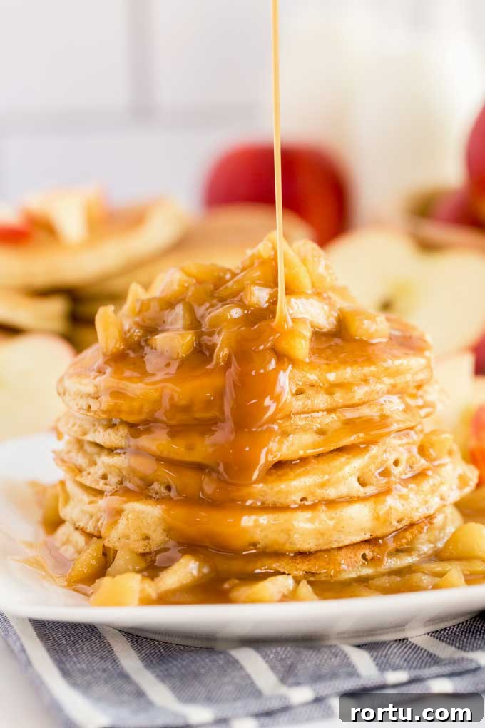 A stack of apple pancakes topped with caramel apples and drizzled with sweet caramel on a white plate