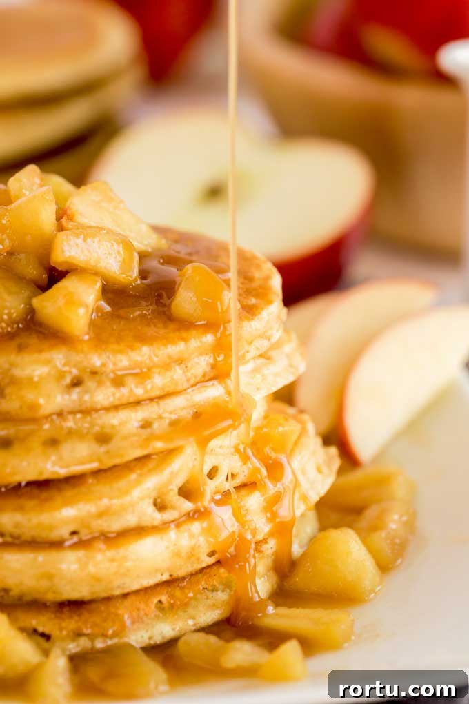 A stack of apple pancakes topped with caramel apples and drizzled with sweet caramel on a white plate