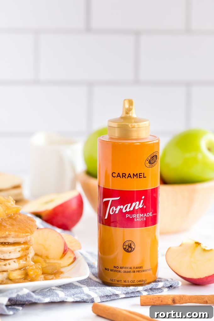 A bottle of Torani Caramel Sauce next to apples, cinnamon and pancakes.