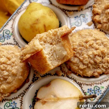 Baked pear muffins in a muffin tin. One sits in the middle with a bite removed.