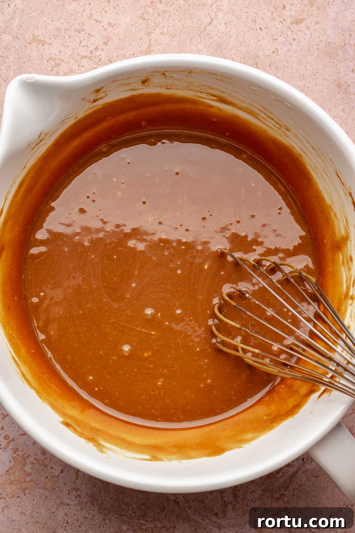 A whisk mixes wet muffin ingredients in a bowl.