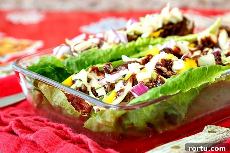 A small, glass rectangular baking dish with carnitas stuffed into Romaine lettuce leaves for lettuce wraps.