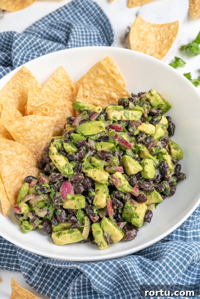 A white bowl with tortilla chips and avocado black bean salsa with pickled red onions and cilantro. 