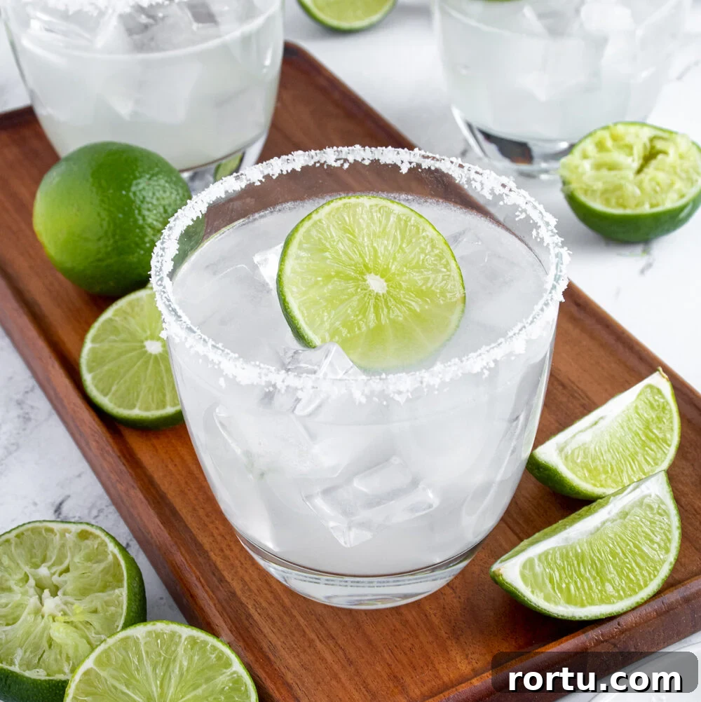 A classic margarita on a wooden platter surrounded by lime halves with a salted rim and a lime wheel as garnish.