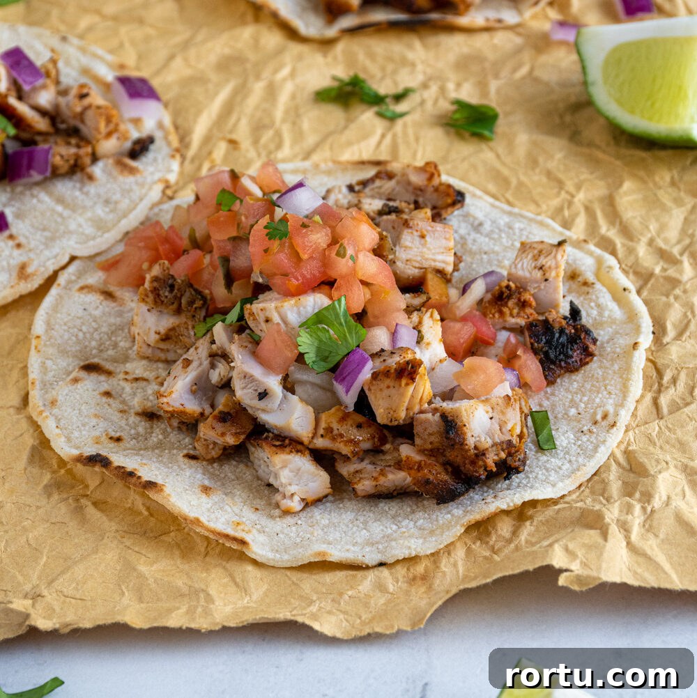 A grilled chicken street taco laid out on a table top filled with chicken and topped with salsa, onions, and cilantro.