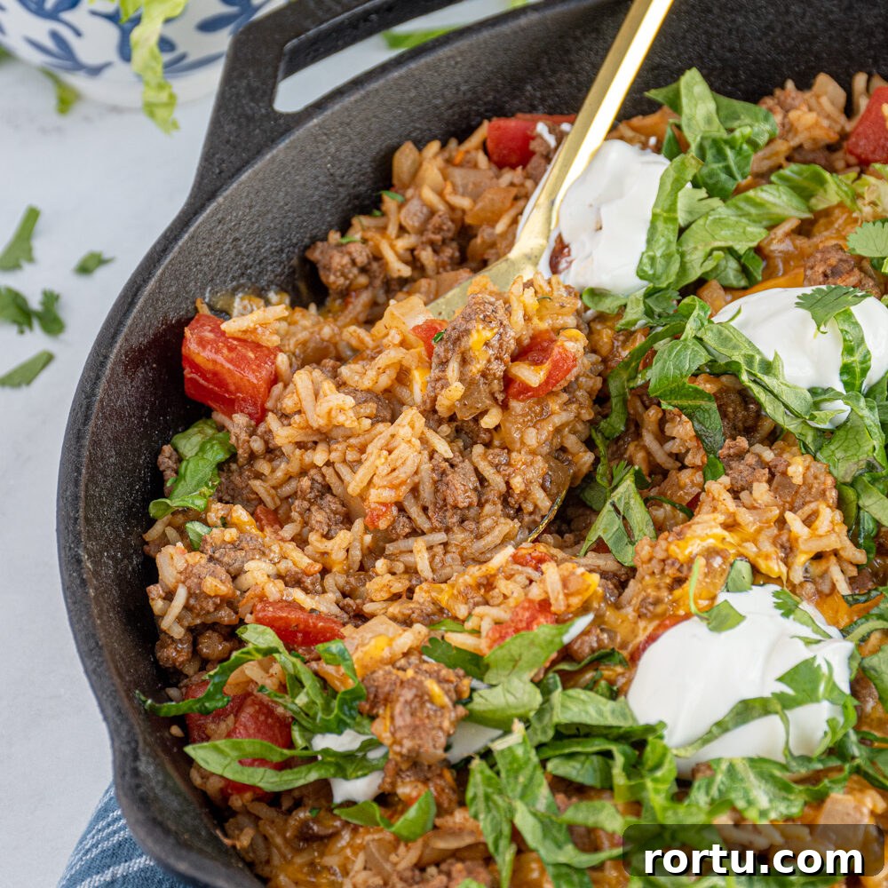 MexicanBeef Taco Rice Skillet in a cast iron pan with a spoon scooping to see the insides with ground beef and rice.
