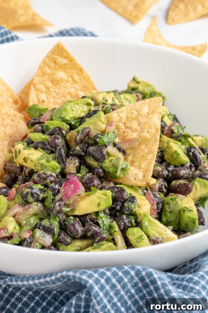 A white bowl with avocado black bean salsa and a tortilla chip full of black beans and avocado chunks.