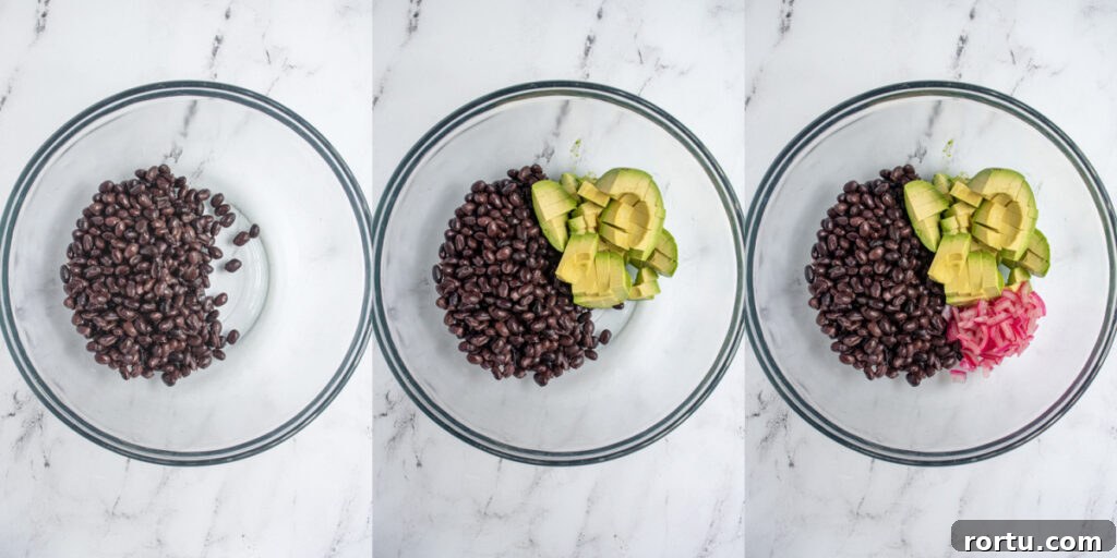 The first steps to making avocado black bean salsa by adding beans, avocado, and pickled red onions to a bowl.