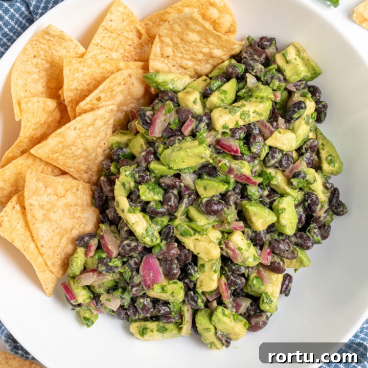 White bowl with avocado black bean salsa and tortilla chips.