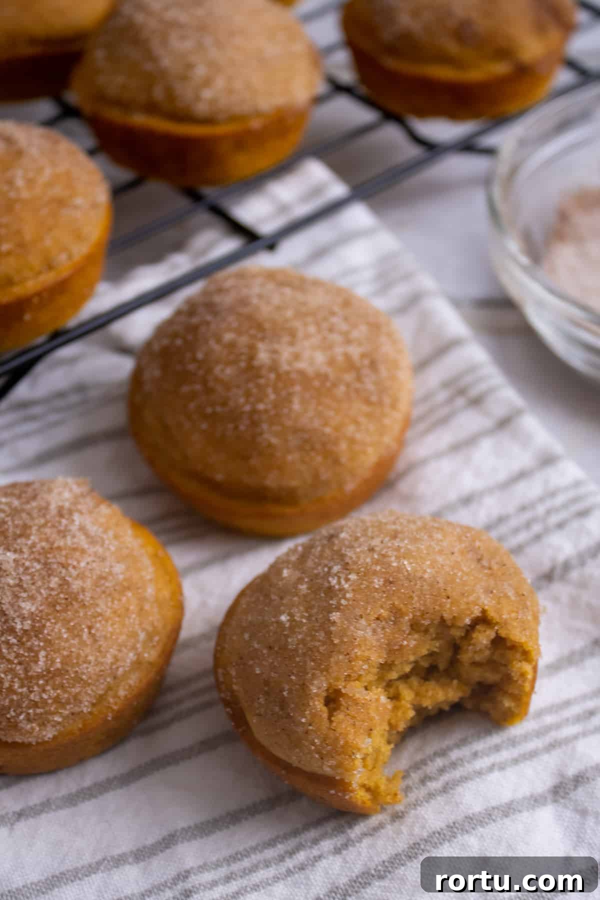 Pumpkin Donut Muffins coated in cinnamon sugar and on a cloth and wire cooling rack.