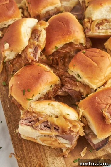Tender Slow-Roasted Eye Round: Juicy, Melts in Your Mouth 11 A close-up of several french dip sliders with beef and onion on a wooden cutting board, topped with chopped herbs.