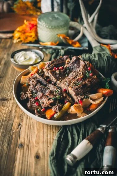 Tender Slow-Roasted Eye Round: Juicy, Melts in Your Mouth 13 A plate of Instant pot chuck roast with carrots, celery, and pomegranate seeds on a wooden table, surrounded by fall decorations and a small bowl of sauce.