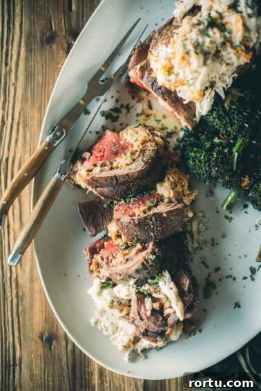Tender Slow-Roasted Eye Round: Juicy, Melts in Your Mouth 14 Sliced beef tenderloin stuffed with crab filling, served with baby broccoli on an oval white plate with a wooden-handled fork.