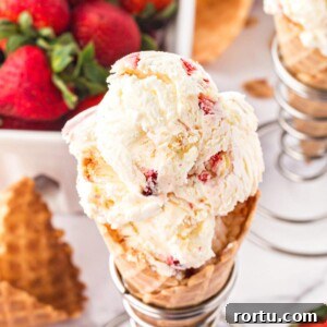 Strawberry Shortcake with a Grown-Up Twist 2 Top view of scooped No-Churn Strawberry Shortcake Ice Cream in a waffle cone with strawberries in the background.