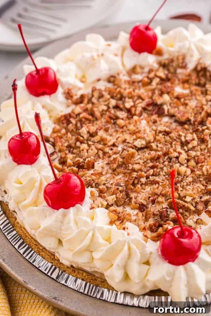 Overhead view of no bake banana split pie topped with chopped pecans, whipped cream, and cherries.