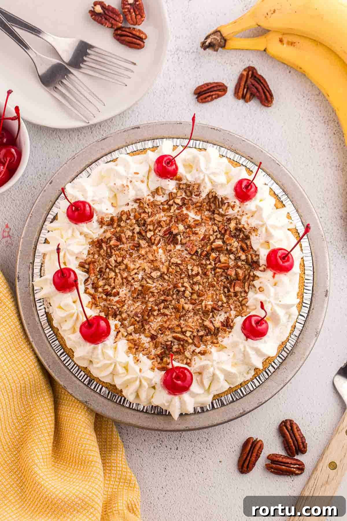 Overhead view of finished no bake banana split pie topped with whipped cream, chopped pecans, and cherries.