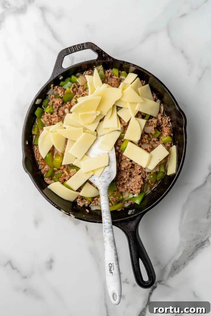 Philly Cheesesteak Sloppy Joes Recipe — Savory Sandwich Twist 6 adding provolone cheese to the sloppy joes in the skillet