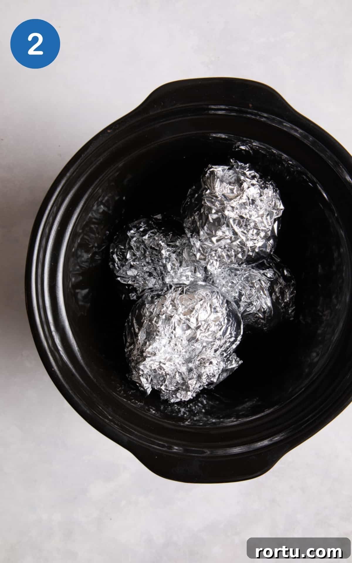 4 jacket potatoes wrapped in foil and placed inside a black slow cooker.