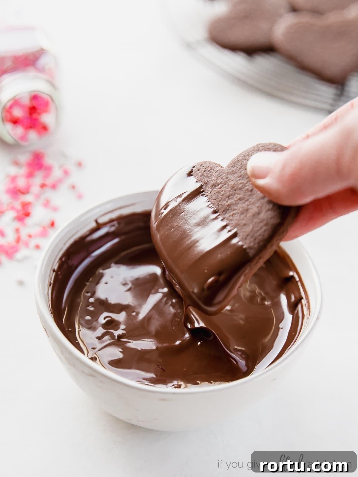 Chocolate Cut-Out Cookies: Perfect Decorated Cocoa Sugar Cookies 6 heart shaped chocolate cookie being dipped in a bowl of melted chocolate
