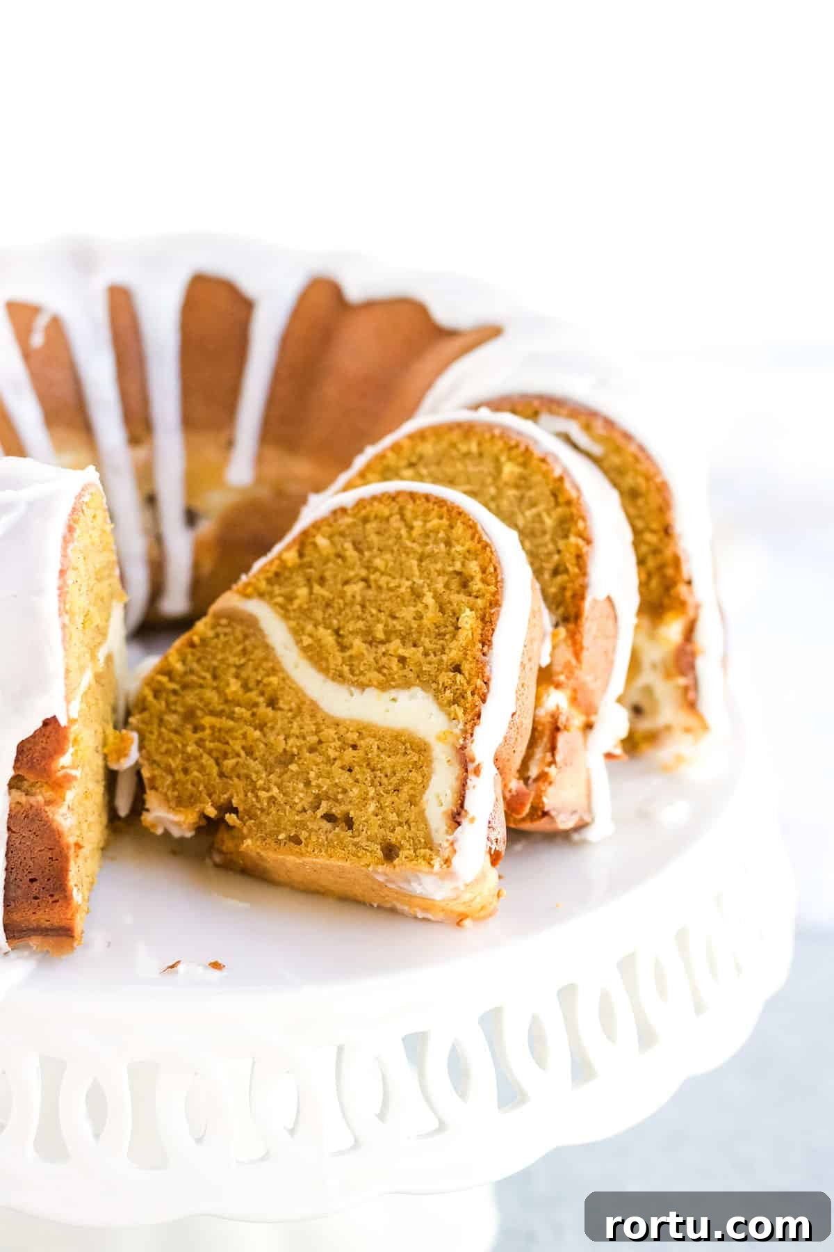 A pumpkin cream cheese pound cake sliced open on a white cake stand.