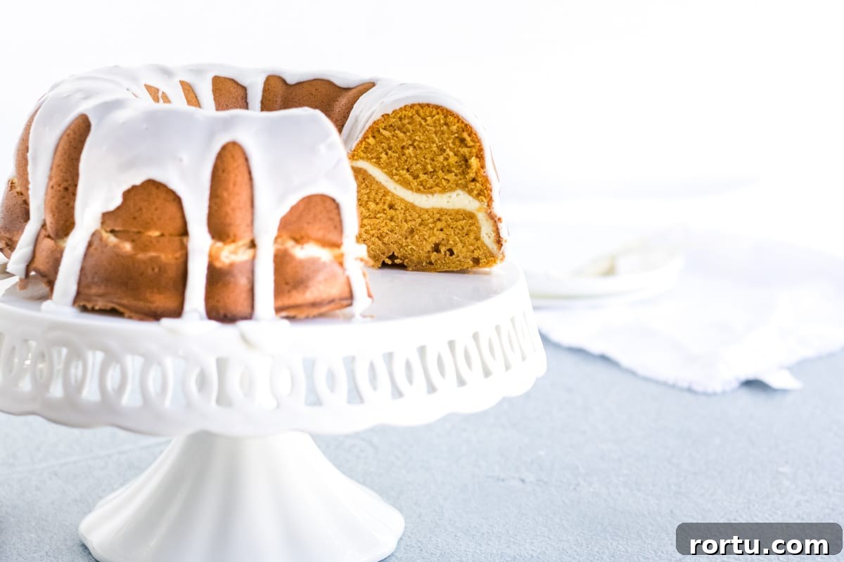 A cream cheese stuffed pumpkin pound cake with a glaze dripping off the sides. 