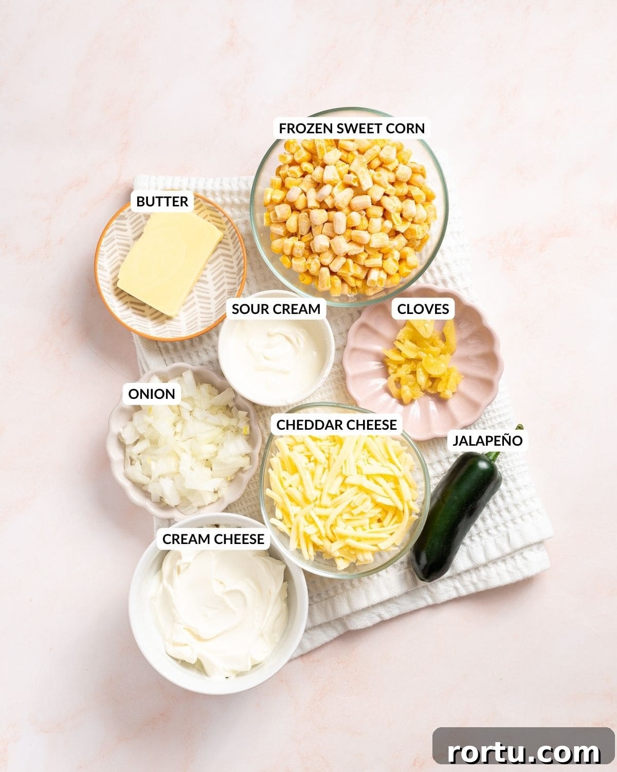 Spicy Jalapeño Corn Salad Bowl 3 An image of the ingredients of jalapeno corn: sweet corn, jalapenos, sour cream, cream cheese, cheddar cheese, butter, garlic cloves, and onions in separate containers with labels.