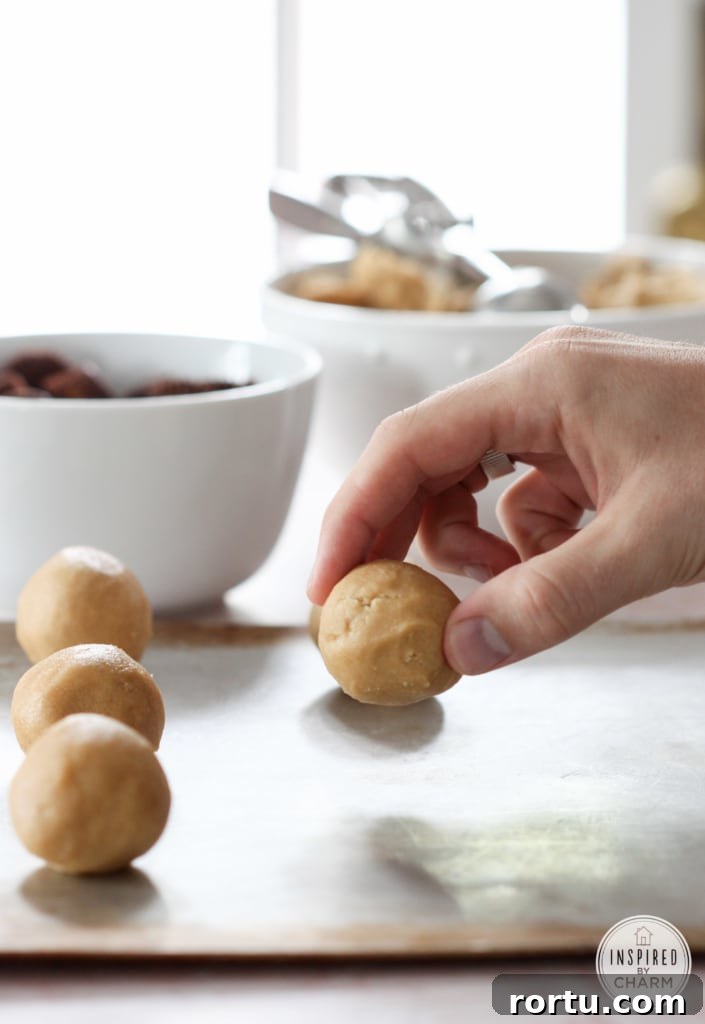hand placing roll peanut butter cookie dough onto a baking sheet.