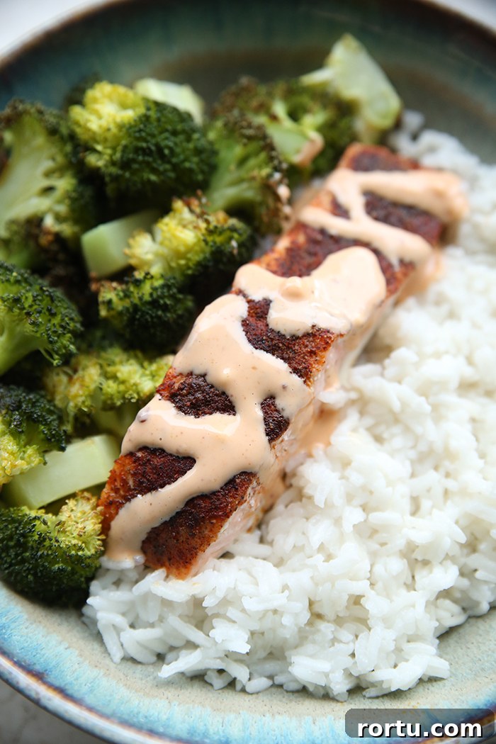 A serving of steamed broccoli, bang bang salmon, and coconut rice on a dinner plate.