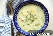A dark blue soup bowl with polkadots filled with clam chowder. On the left of the bowl is a checkered patterned kitchen towel with a spoon sitting on top.