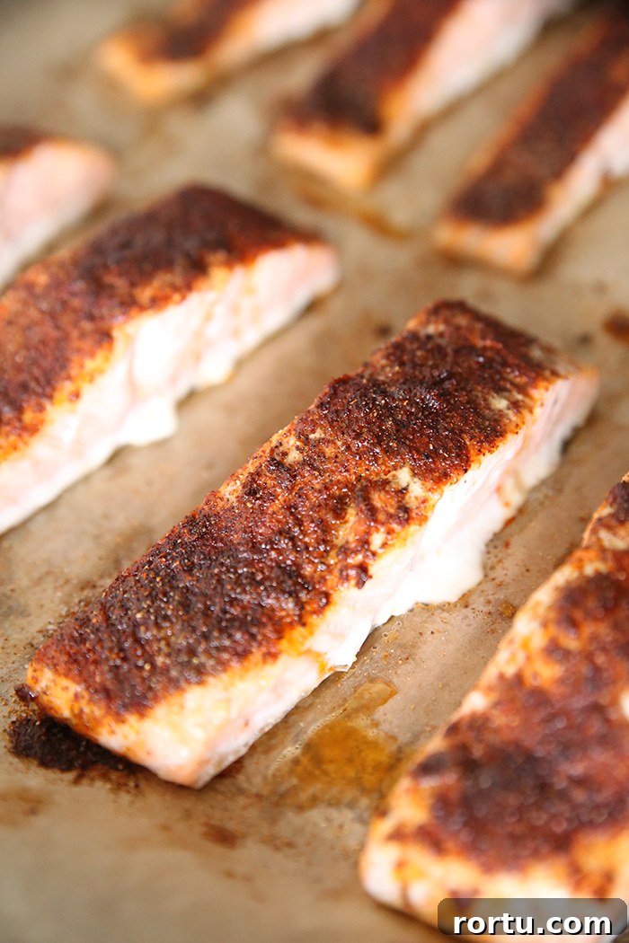 A baking sheet covered with brown parchment paper and several pieces of baked salmon with a spice rub on top.