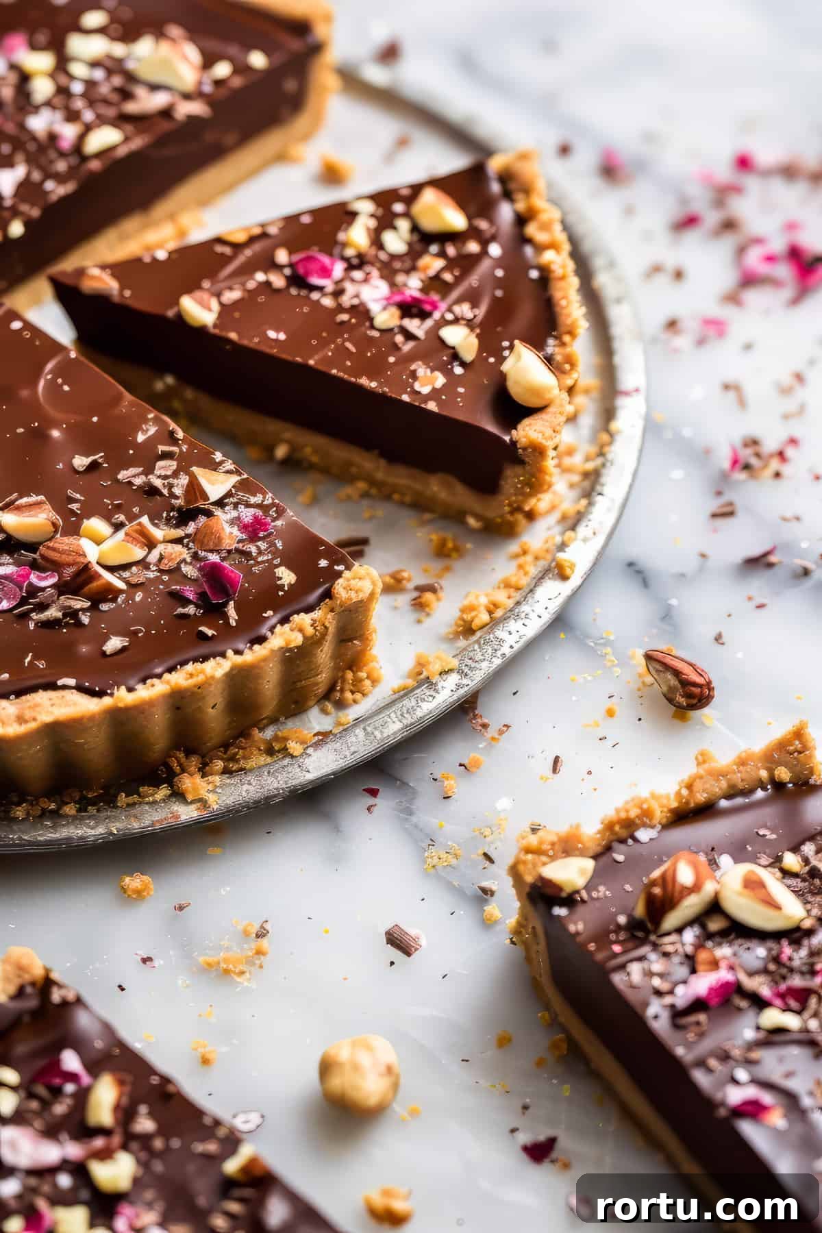 Chocolate hazelnut tart on a marble cake plate with chopped hazelnuts.