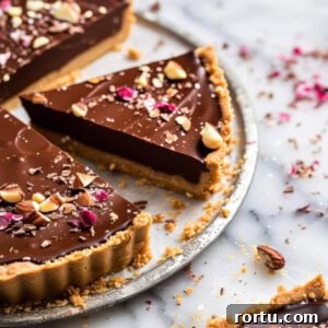 Chocolate hazelnut tart on a marble cake plate with chopped hazelnuts.