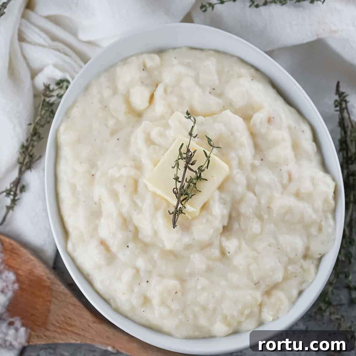 Overhead shot of parsnip and potato mash with a pad of butter and herbs in a white bowl with a wooden spoon on the side.