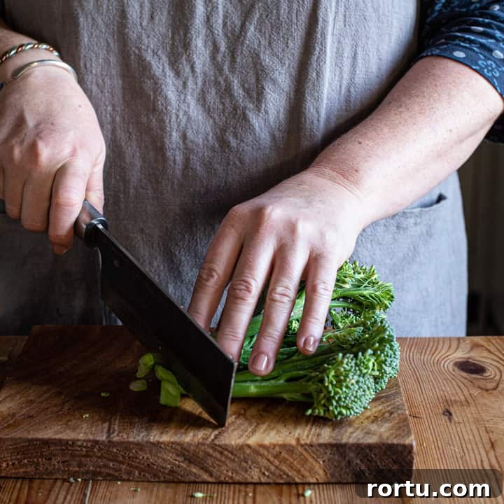 womans hands chopping broccoli on a wooden board with large Japanese knife