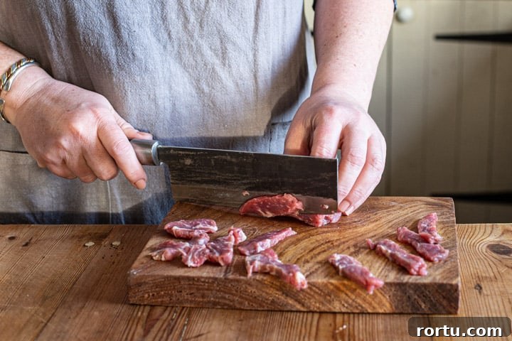 womans hands chopping sirloin steak on a wooden board with large Japanese knife