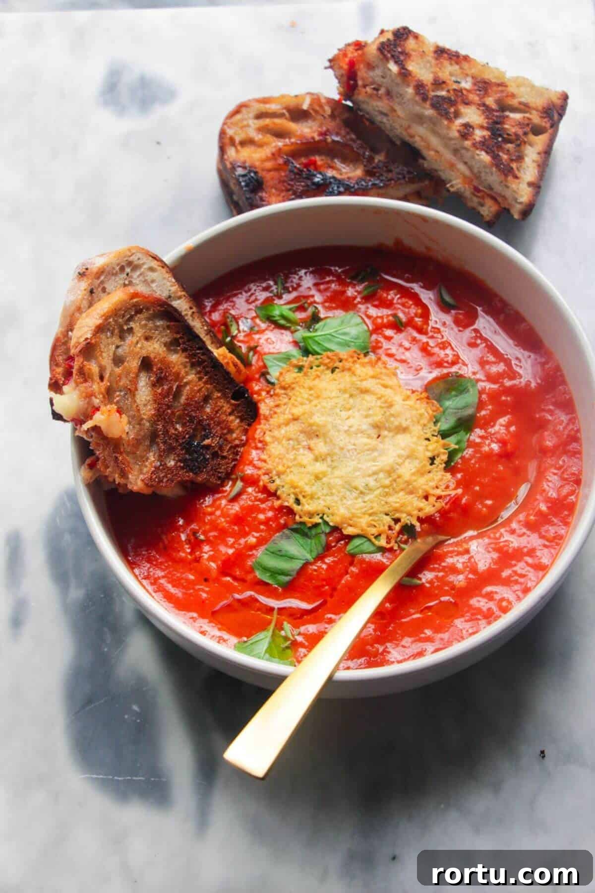 Roasted red pepper and tomato soup in a white bowl with grilled cheese dipped in.