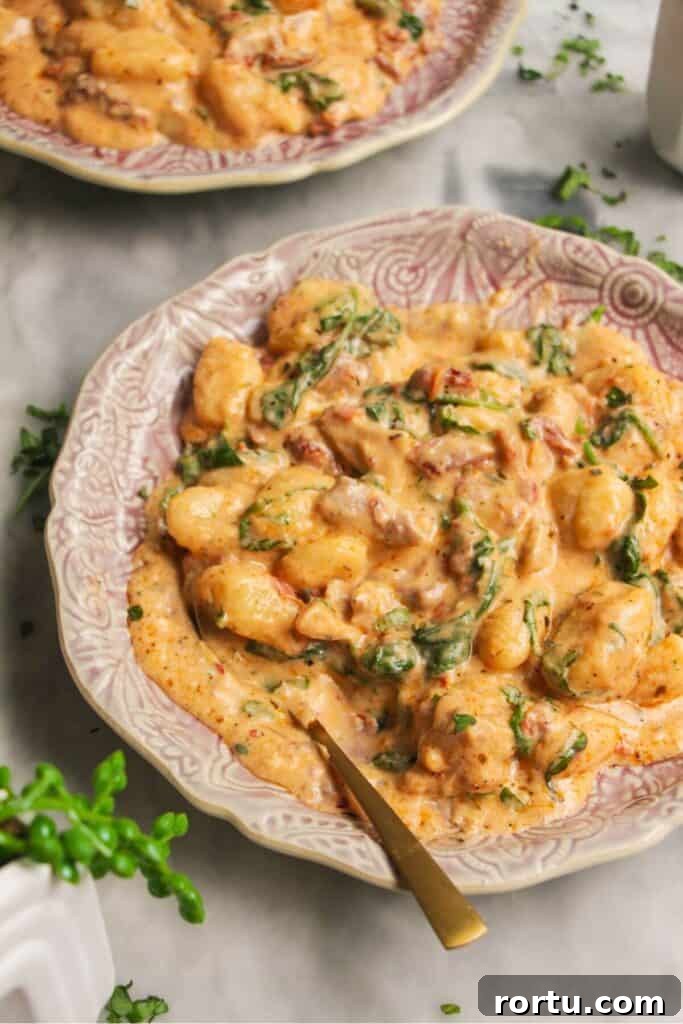 Close up of creamy chicken gnocchi on a small pink plate with another plate in the background.